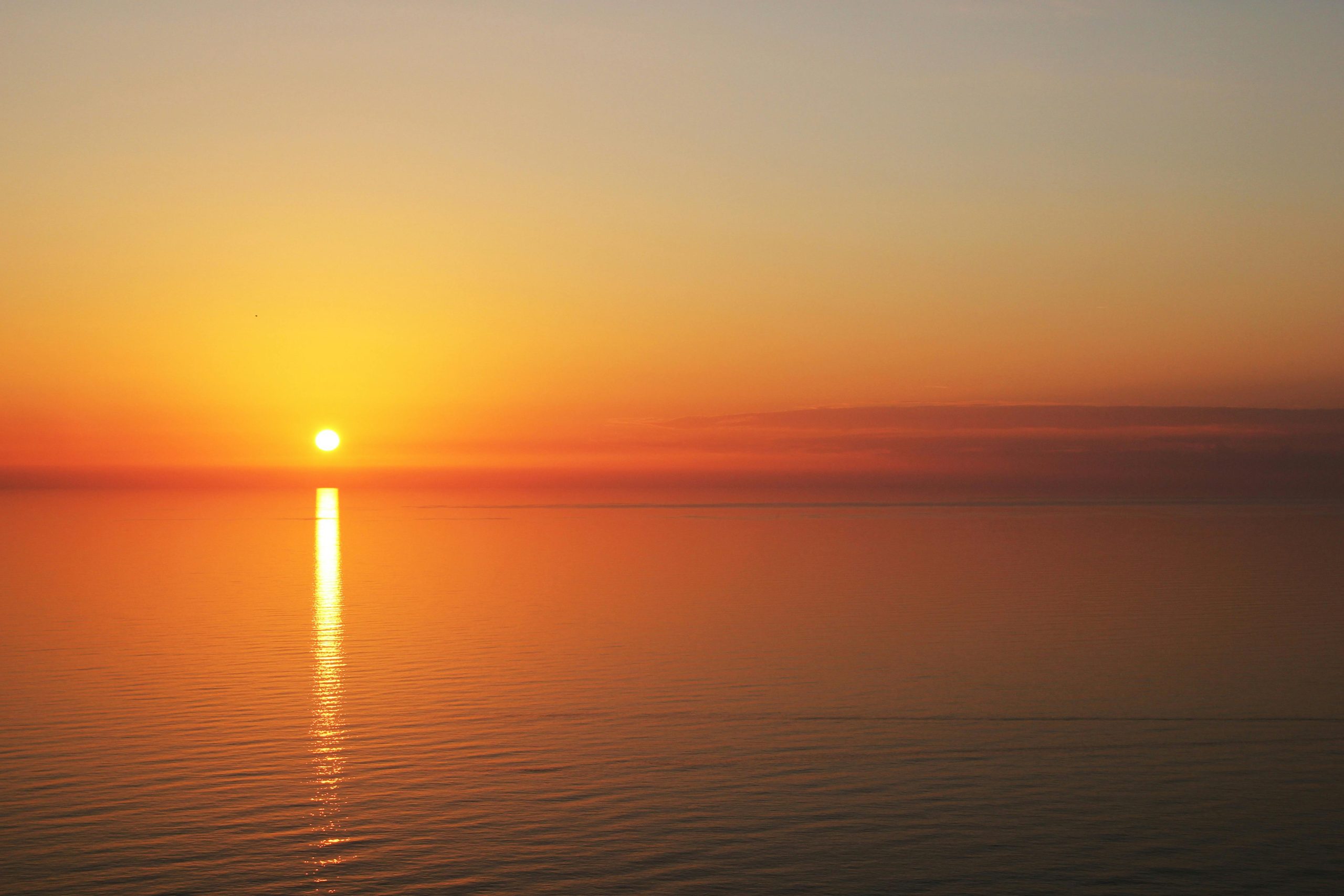 coucher de soleil avec toutes les nuances de couleur (jaune, orange, bleu, gris). l'image est prise en bord de mer. reflet du soleil sur l'eau.